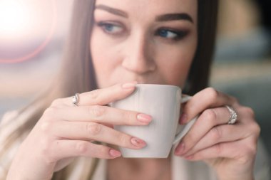 Beyaz ceketli genç bir kadın kafeteryada çalışıyor, kahve içiyor.
