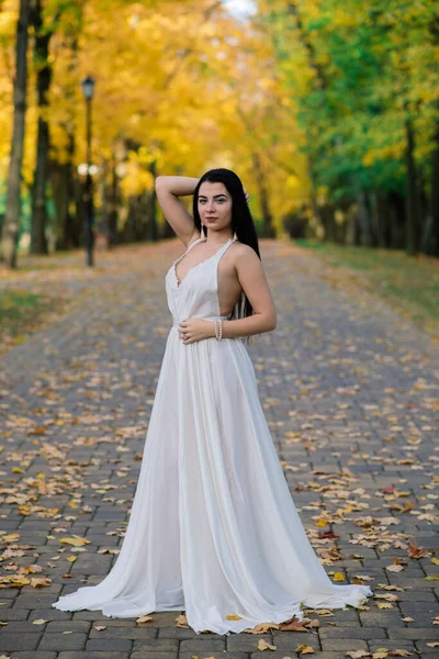 Güz parkında beyaz elbiseli güzel esmer bir kadın.