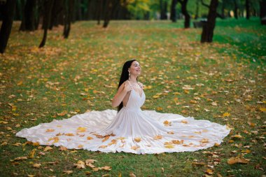 Güz parkında beyaz elbiseli güzel esmer bir kadın.
