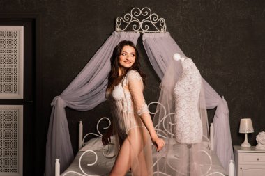 Beyaz iç çamaşırlı güzel gelin yatak odasında ve stüdyosunda oturuyor. Düğün konsepti sabahı