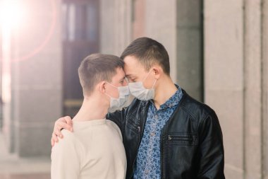 Tıbbi maske takan, şehirde sarılıp öpüşen genç eşcinsel çift..