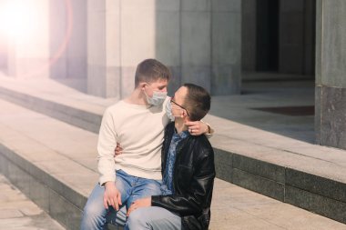 Tıbbi maske takan, şehirde sarılıp öpüşen genç eşcinsel çift..