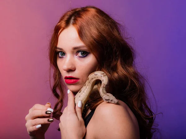 Beautiful young redhead woman with snake with a fashionable perfect makeup. Studio shot, neon light