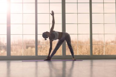 Genç, çekici, gülümseyen bir kadın yoga yapıyor, spor kıyafetleri giyiyor, sutyen giyiyor, evde eğitim görüyor.