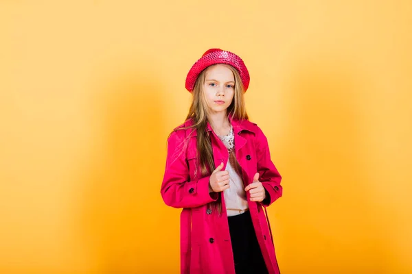 Portrait of happy girl in a raincoat and boots standing on yellow background