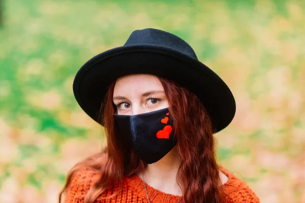 穿着针织红毛衣 头戴黑色时髦口罩的年轻女子在秋天的黄色公园里的画像 生活方式 — 图库照片
