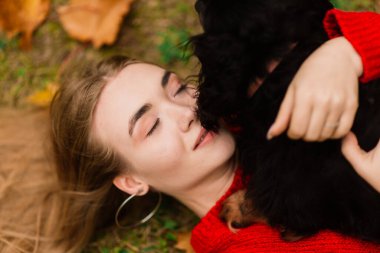 Sonbahar parkında küçük köpeğini kucağında tutan mutlu kadın.