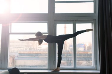 Genç, çekici, gülümseyen bir kadın yoga yapıyor, spor kıyafetleri giyiyor, sutyen giyiyor, evde eğitim görüyor.