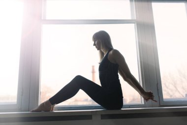 Genç, çekici, gülümseyen bir kadın yoga yapıyor, spor kıyafetleri giyiyor, sutyen giyiyor, evde eğitim görüyor.