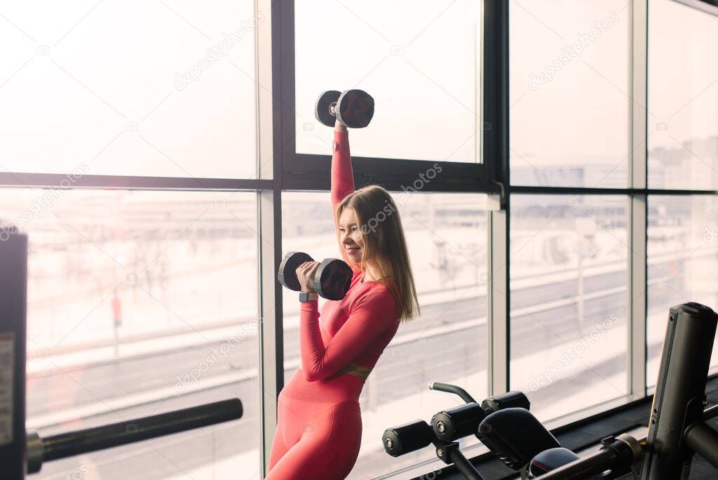 Sporty woman in a gym, dumbbells, barbell, smiling and fitness