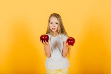 Stüdyoda kırmızı elmalı güzel sarışın kız, sarı arka plan.