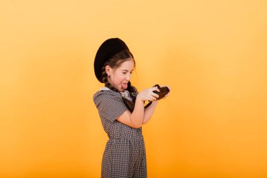 Küçük tatlı bir kız sarı arka planda fotoğraf çekiyor..