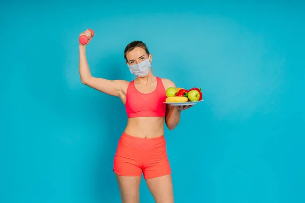 Woman in a face protection mask and fitness wear isolated over blue background.