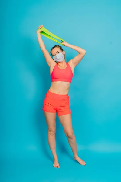 Woman in a face protection mask and fitness wear isolated over blue background.