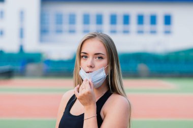 Sahada koruyucu maskeyle oynayan bayan tenisçi