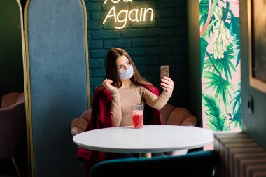 Tıbbi maske takan, sokakta ve kafede dikilen beyaz kadın portresi.