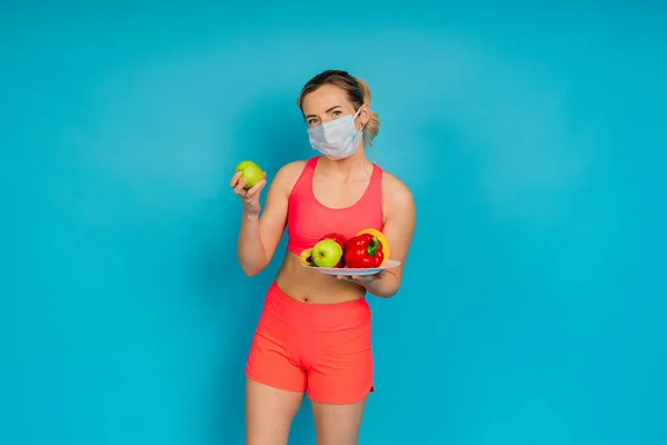 Woman in a face protection mask and fitness wear isolated over blue background.