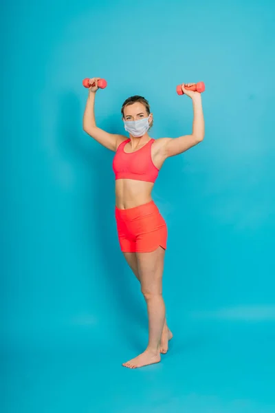 Woman in a face protection mask and fitness wear isolated over blue background.