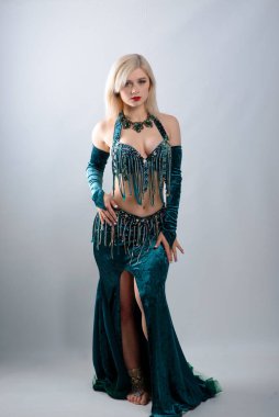 Genç, güzel, egzotik, doğulu kadın beyaz arka planda yeşil bir elbiseyle göbek dansı yapıyor..