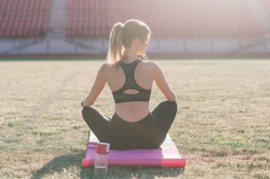 Genç bir bayan stadyumda yoga yapıyor.