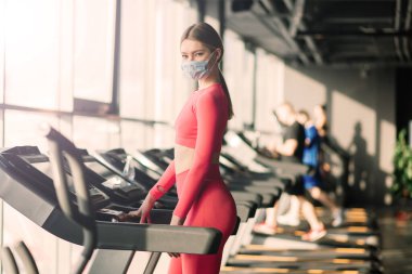 Coronavirus covid-19 önleme, sağlık maskeli spor salonunda poz veren fitness kızı. Savaşan virüsler.