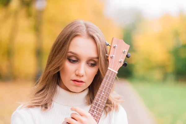 美しい女性は秋の森の中で屋外でウクレレギターを演奏 — ストック写真