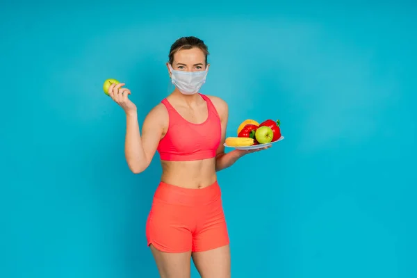 Woman in a face protection mask and fitness wear isolated over blue background.
