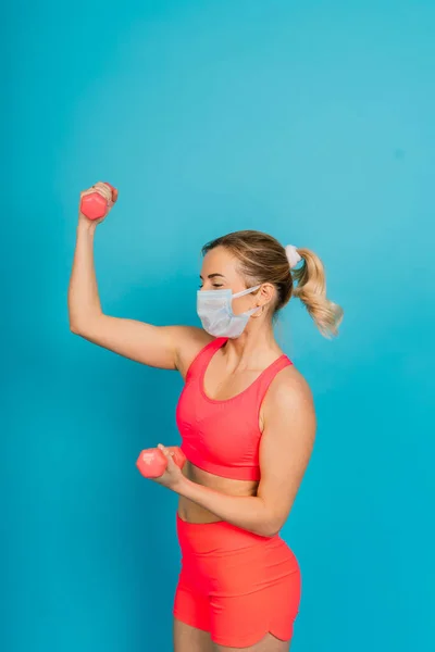 Woman in a face protection mask and fitness wear isolated over blue background.