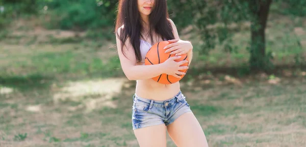 若い運動選手の女性は トップとスウェットパンツで 屋外のバスケットボールコートでボールと遊ぶ — ストック写真