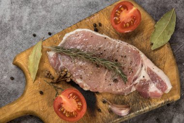 Taze et, kesme tahtasında domuz karbonatı, domatesler ve gri noktalı arka planda baharatlar