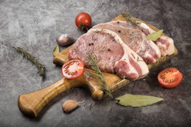 Taze et, kesme tahtasında domuz karbonatı, domatesler ve gri noktalı arka planda baharatlar