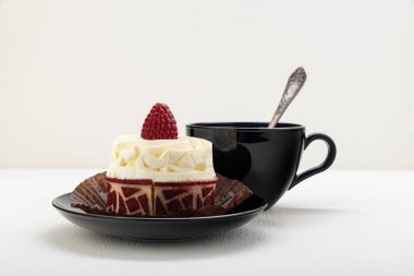 Kremalı ve ahududulu kek sepeti, bir fincan çayla birlikte siyah bir çay tabağının üzerinde. hafif bir arkaplanda