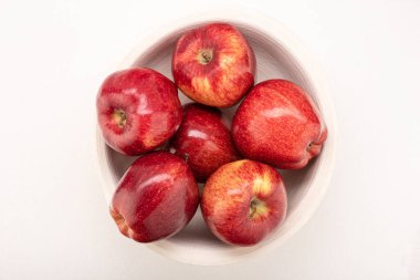 Elmalar kırmızı-sarıdır, hafif bir arka planda açık ahşap bir kasede suludur.