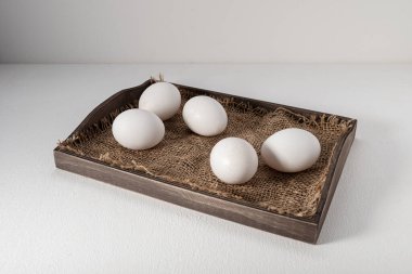 Beyaz kabuklu yumurtalar, tahta tepside ve beyaz arka planda.