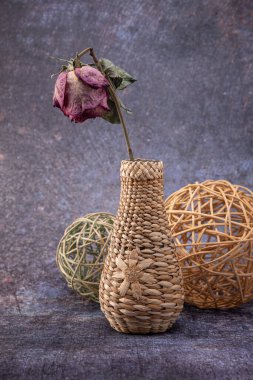 Kuru bir gül, hasır bir vazoda, ve renkli, koyu bir arka planda hasır toplar