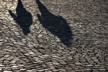 Antik kaldırımlardaki insanların gölgeleri, güneş parlıyor.