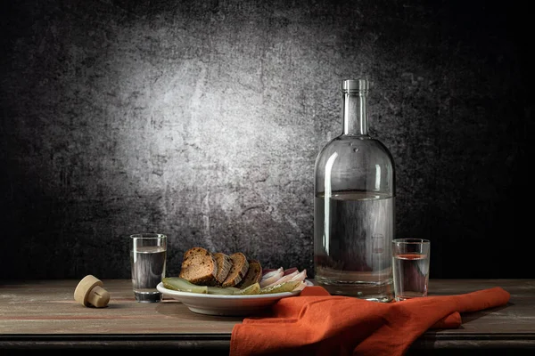 一只玻璃瓶 两只玻璃杯 一杯浓烈的饮料 一只白色的盘子 上面有零食 一张红色的餐巾 放在木制桌面上 背景上有污迹 图库图片