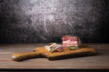 Appetizer on a cutting board, sliced lard, with bay leaf, on a wooden countertop, on a gray background