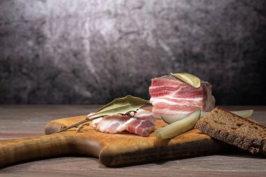 Appetizer on a cutting board, sliced lard, with bay leaf, on a wooden countertop, on a gray background