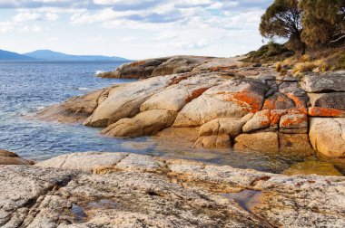 Litenlerle kırmızıya boyanmış granit kayalar dalgalarla pürüzsüz cilalanır - Swansea, Tazmanya, Avustralya