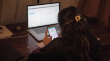 Kadın dijital bilgisayar ve akıllı telefon kullanarak çevrimiçi görüntülü konuşma yapıyor, oturma odasında oturuyor.