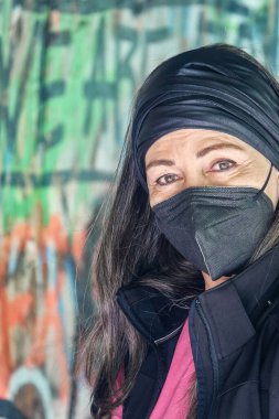  Arkasında duvar yazısı olan, gri saçlı, balkabağı koruyucu maskeli, 50 'li yaşlarda çekici bir kadının portresi.                                  