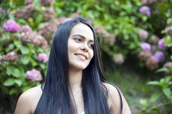 笑容满面的年轻的拉丁裔美国女人的画像 孤零零的树木和花朵的背景 积极的人类情感 — 图库照片