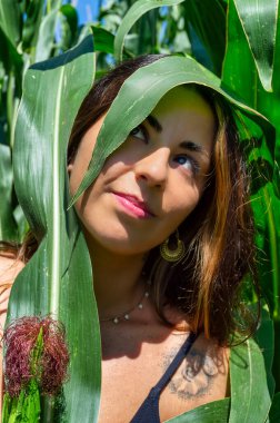 Güneşli bir günde yeşil tarla bitkilerinin arasında duran genç bir kadının portresi. Çiftçiliği, doğayı, sürdürülebilirliği ve kırsal yaşamı temsil eden doğal yaşam tarzı.