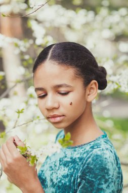 Etrafı çiçek açan ağaçlarla çevrili güzel bir kız. Baharda yanağında bir uğur böceğiyle.