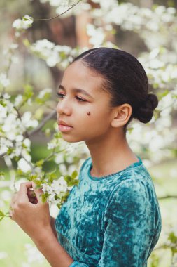 Baharda çiçek açan ağaçlarla çevrili yüzünde uğur böceği olan güzel bir kız.