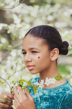 Baharda çiçek açan ağaçlarla çevrili yüzünde uğur böceği olan güzel bir kız.