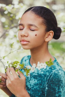 Baharda çiçek açan ağaçlarla çevrili yüzünde uğur böceği olan güzel bir kız.