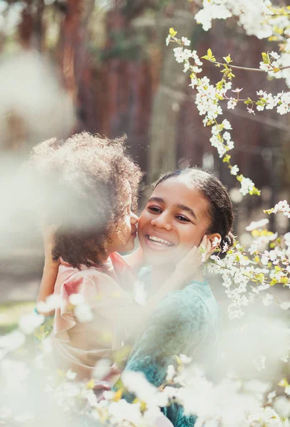 Sweet family portrait of two little sisters in springtime garden. Little girl give a kiss to her elder sister — Stock Image Sweet Family Portrait Two Little Sisters Springtime Garden Little Girl Royalty Free Stock Images
