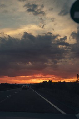 Gün batımında gökyüzü ile ufukta asfalt yol. Bazı kuşlar tam boy çekimde görülebilir.